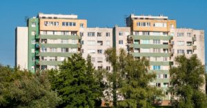 High-rise apartment buildings surrounded by trees under a clear blue sky.